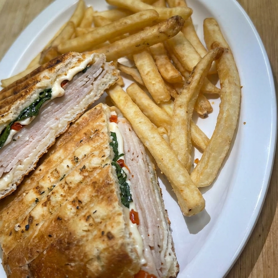 Grilled chicken and vegetable pita sandwich with French fries on a white plate atop a wooden table.