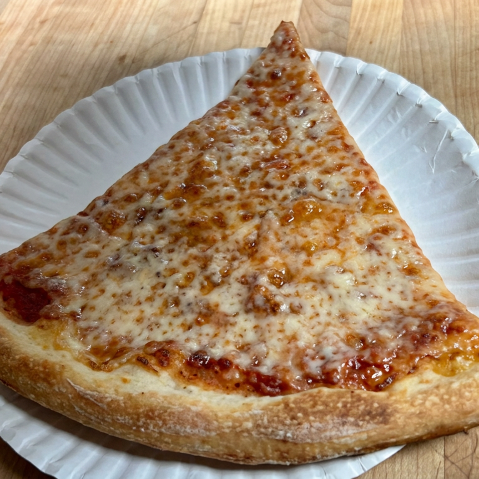 Large triangular slice of cheese pizza on a white paper plate atop a wooden table.